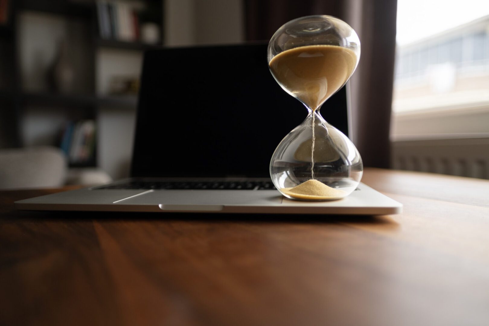 Hourglass on table, sand flowing through the bulb of sandglass, time is money concept, times passing concept like work or business deadline, resemble urgency running out of occasion in life